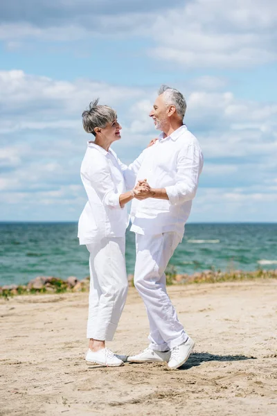 Ganzkörperansicht glücklicher Senioren, die sich beim Tanzen am Strand anschauen — Stockfoto