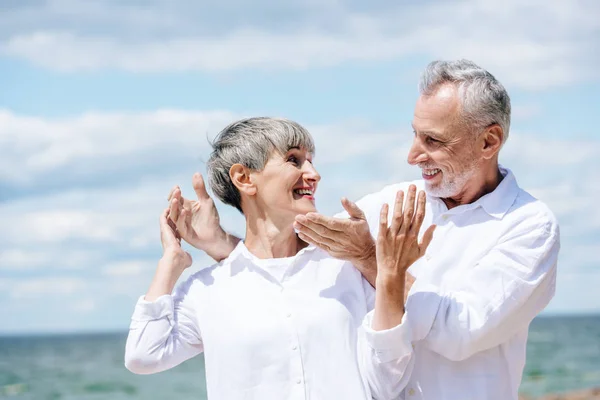 Feliz pareja de ancianos en camisas blancas de pie bajo el cielo azul en el día soleado - foto de stock