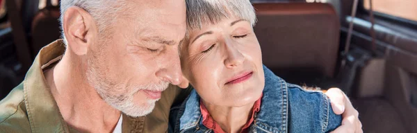 Panoramablick auf ein älteres Paar, das sich mit geschlossenen Augen im Auto umarmt — Stockfoto