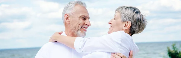 Vista panorâmica do homem sênior sorrindo levantando esposa sob o céu azul — Fotografia de Stock