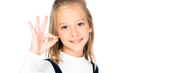 Plano panorámico de la colegiala sonriente mostrando gesto ok mientras mira la cámara aislada en blanco - foto de stock