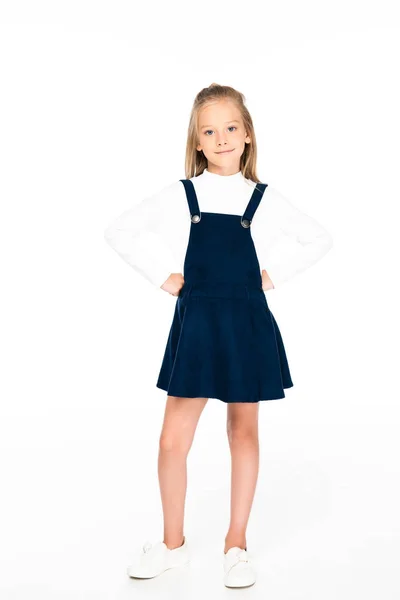 Full length view of cute schoolgirl holding hands on hips while posing at camera on white background — Stock Photo