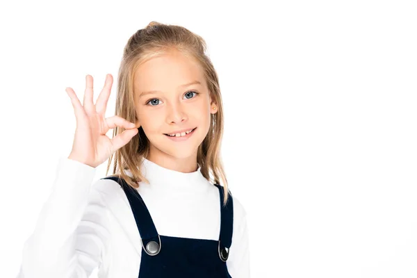 Entzückendes, lächelndes Schulmädchen, das ok Geste zeigt, während es isoliert auf weiß in die Kamera schaut — Stockfoto