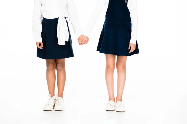 Обрезанный вид двух мультикультурных школьниц, держащихся за руки на белом фоне — стоковое фото