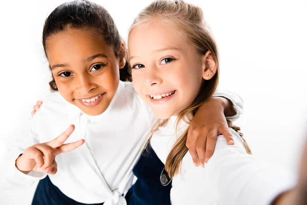 Selektiver Fokus der fröhlichen afrikanisch-amerikanischen Schülerin, die Siegeszeichen zeigt, während sie Freundin isoliert auf Weiß umarmt — Stockfoto