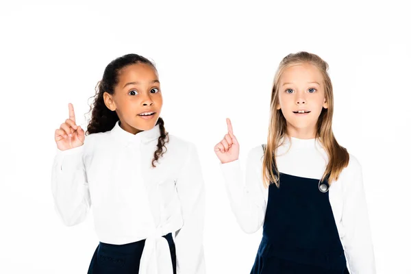 Two smiling multicultural schoolgirls showing idea gestures while looking at camera isolated on white — Stock Photo