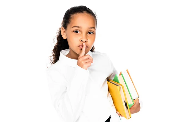 Adorable african american schoolgirl holding books and showing hush gesture isolated on white — Stock Photo