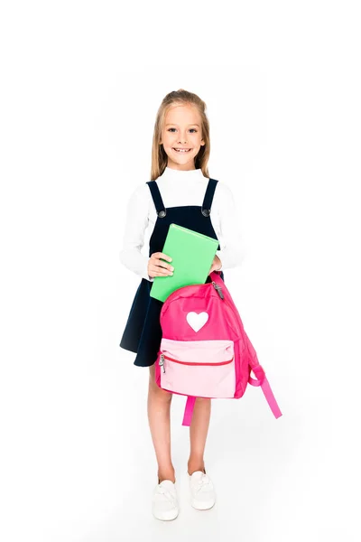 Full length view of cute schoolgirl holding backpack and book on white background — Stock Photo