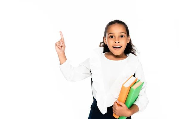 Joyeuse écolière afro-américaine pointant du doigt tout en tenant des livres isolés sur blanc — Photo de stock