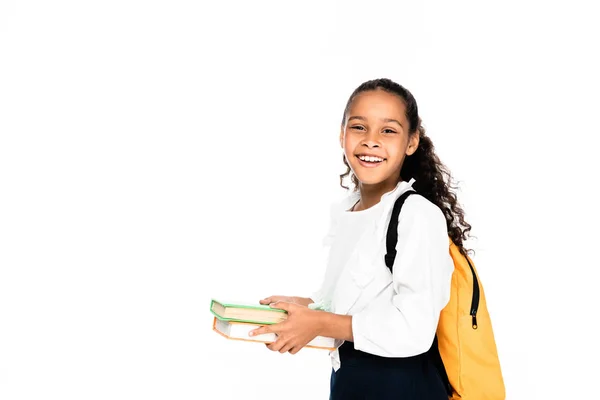 Happy afrcan american schoolgirl smiling at camera while holding books isolated on white — Stock Photo