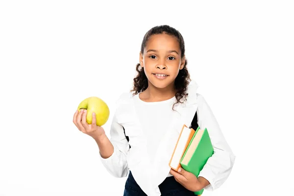 Adorable african american schoolgirls looking at camera while holding books and apple isolated on white — Stock Photo