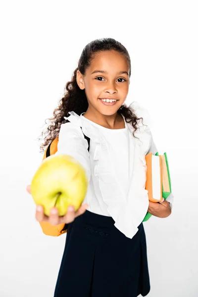 Selective focus of african american schoolgirl showing apple while holding books on white background — Stock Photo