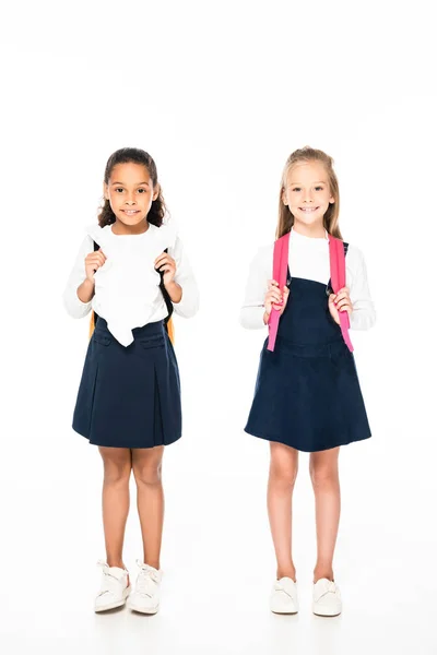 Full length view of two adorable multicultural schoolgirls smiling at camera on white background — Stock Photo