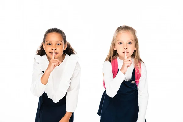 Two adorable multicultural schoolgirls showing hush gestures isolated on white — Stock Photo