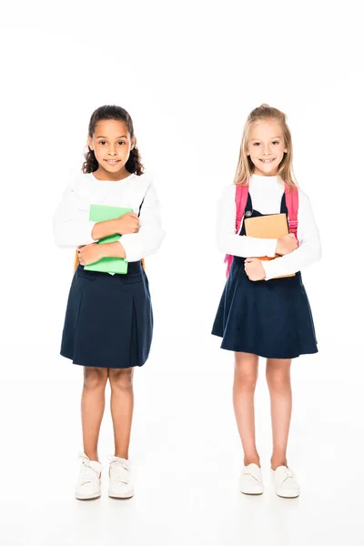 Full length view of two adorable multicultural schoolgirls holding books on white background — Stock Photo