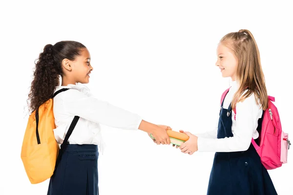 Side view of cheerful african american schoolgirl giving books to smiling friend isolated on white — Stock Photo