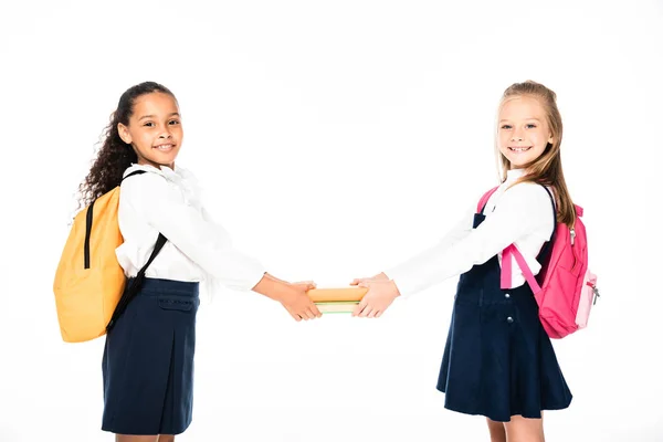 Two cheerful multicultural schoolgirls holding books together isolated on white — Stock Photo