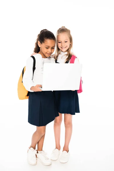 Full length view of two multicultural schoolgirls using laptop isolated on white — Stock Photo