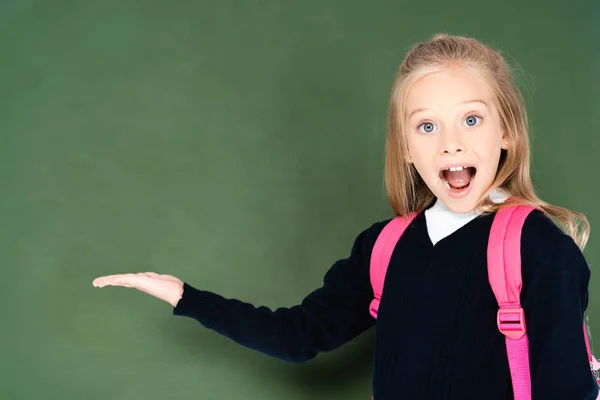 Colegiala emocionada mirando a la cámara mientras está de pie cerca de pizarra verde - foto de stock