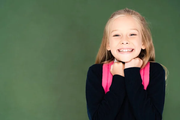 Niedliches, glückliches Schulmädchen, das in die Kamera lächelt, während es neben der grünen Kreidetafel steht — Stockfoto