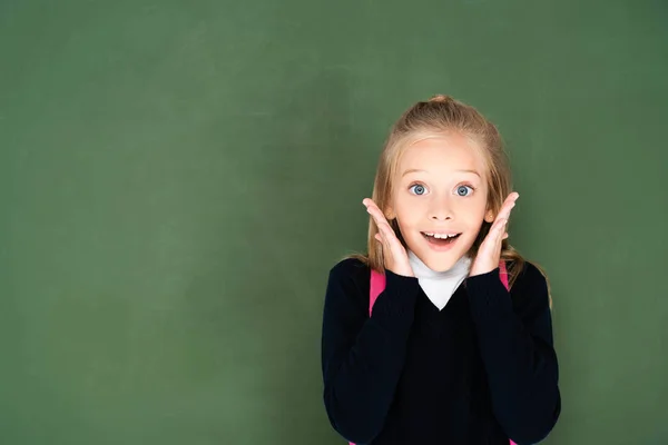 Colegiala emocionada sonriendo a la cámara mientras está de pie cerca de pizarra verde - foto de stock