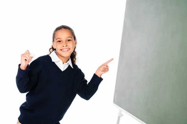 Fröhliche afrikanisch-amerikanische Schülerin zeigt mit dem Finger auf grüne Kreidetafel isoliert auf weiß — Stockfoto