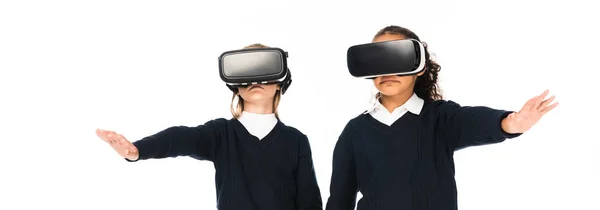 Panoramic shot of two multicultural schoolgirls using virtual reality headsets isolated on white — Stock Photo