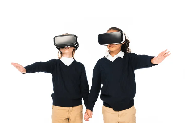 Zwei multikulturelle Schulmädchen halten sich an den Händen, während sie Virtual-Reality-Headsets isoliert auf weiß verwenden — Stockfoto