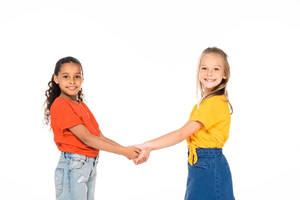 Two cute multicultural friends holding hands and smiling at camera isolated on white — Stock Photo