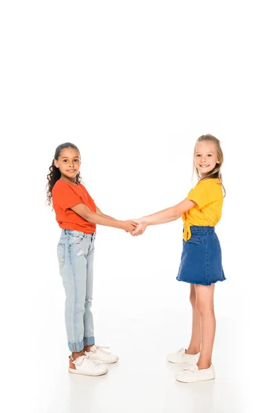 Vue pleine longueur de deux amis multiculturels mignons tenant la main et souriant à la caméra sur fond blanc — Photo de stock