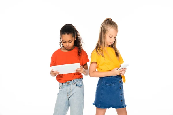 Dos amigos multiculturales atentos utilizando smartphone y tableta digital aislados en blanco - foto de stock