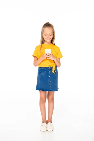 Vista completa de un niño lindo y sonriente usando un teléfono inteligente sobre un fondo blanco - foto de stock