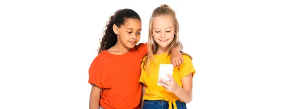 Plano panorámico de lindo africano americano niño abrazando amigo usando teléfono inteligente aislado en blanco - foto de stock
