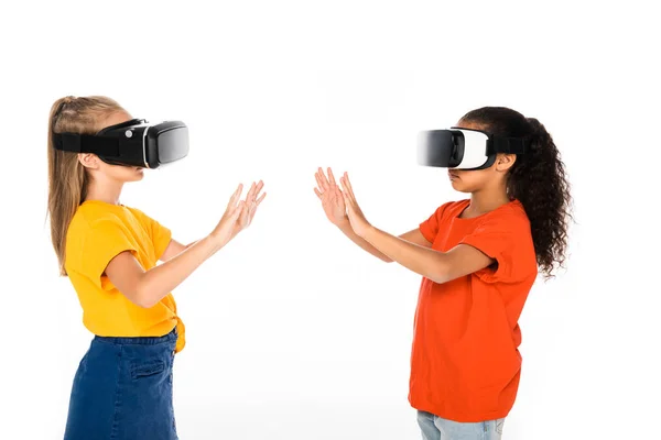 Dos amigos multiculturales mirándose entre sí mientras usan auriculares de realidad virtual aislados en blanco - foto de stock