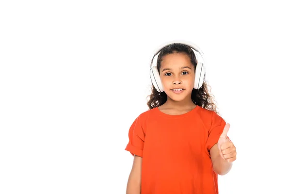 Lindo africano americano niño mostrando pulgar hacia arriba mientras escucha música en auriculares aislados en blanco - foto de stock