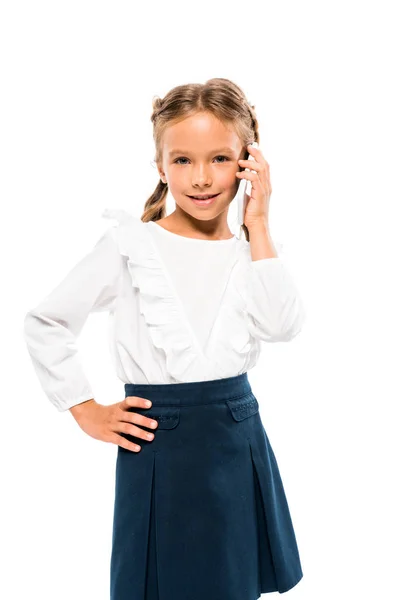 Lindo niño de pie con la mano en la cadera y hablando en el teléfono inteligente aislado en blanco - foto de stock