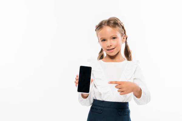 Niño feliz apuntando con el dedo al teléfono inteligente con pantalla en blanco aislado en blanco - foto de stock