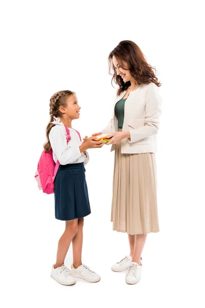 Feliz madre sosteniendo libros cerca de hija con mochila aislada en blanco - foto de stock