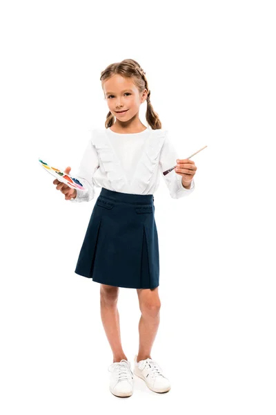 Niño positivo sosteniendo colorida paleta de acuarela aislado en blanco - foto de stock
