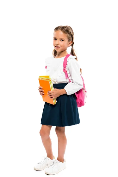 Criança alegre que prende livros e que está com a mochila rosa isolada no branco — Fotografia de Stock