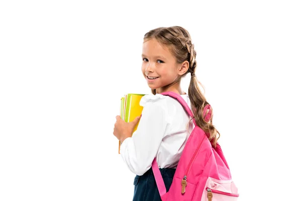 Criança sorridente de pé com mochila rosa e livros isolados em branco — Fotografia de Stock