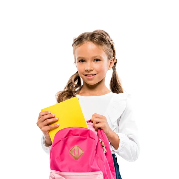 Lächelndes Kind legt Buch in rosa Rucksack isoliert auf weiß — Stockfoto