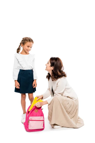 Glückliche Mutter legt Buch in Rucksack der glücklichen Tochter isoliert auf weiß — Stockfoto