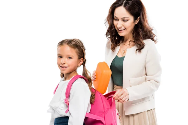 Mãe atraente colocando lancheira na mochila da filha bonito isolado no branco — Fotografia de Stock