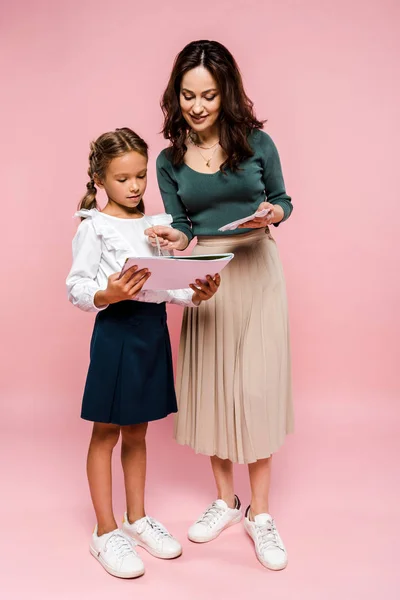 Feliz madre de pie cerca de la hija y la pintura en rosa - foto de stock