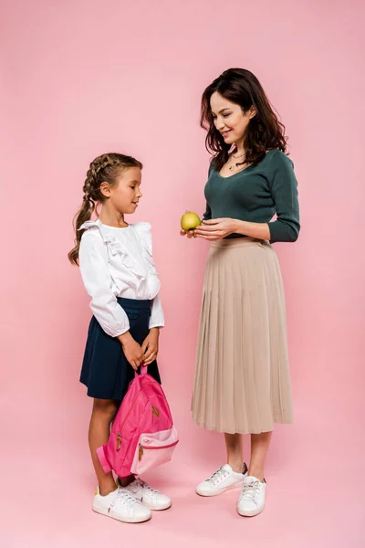 Mãe segurando maçã saborosa perto da filha com mochila em rosa — Fotografia de Stock