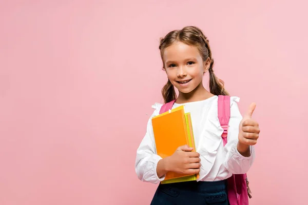 Criança feliz segurando livros e mostrando polegar para cima isolado em rosa — Fotografia de Stock