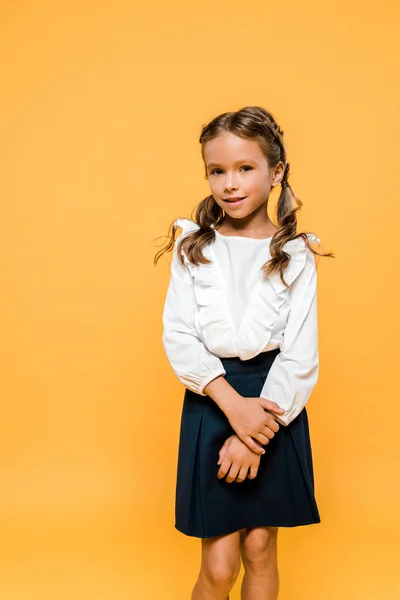 Feliz colegiala sonriendo y de pie aislado en naranja - foto de stock