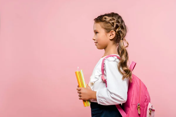 Seitenansicht eines glücklichen Kindes, das Bücher hält, während es mit Rucksack isoliert auf rosa steht — Stockfoto