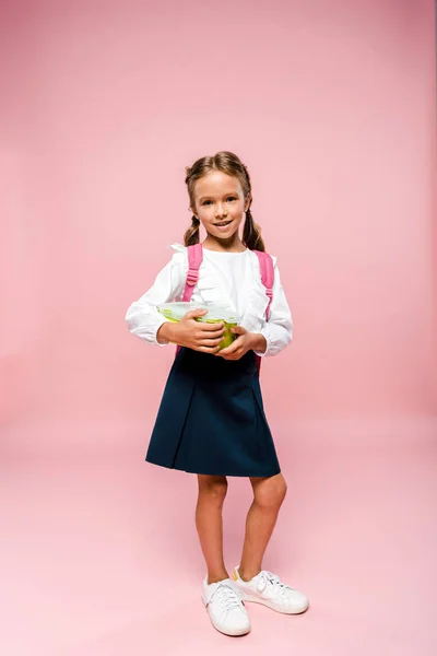 Glückliches Kind hält Lunchbox und steht auf rosa — Stockfoto